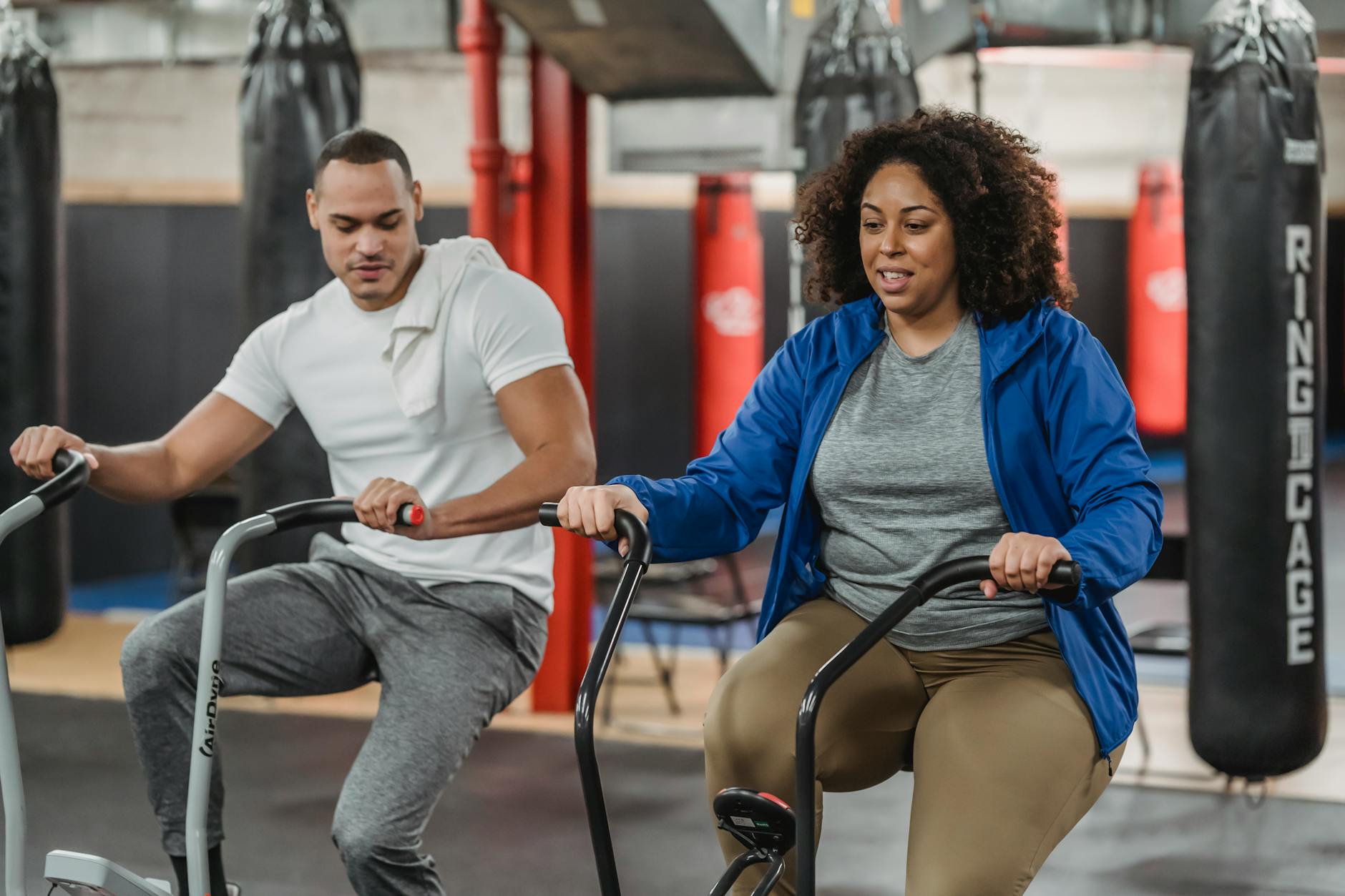 Trening siłowy i cardio w jednym planie: jak skutecznie łączyć je na siłowni MEDIGYM Trener wspiera ćwiczącą na rowerku stacjonarnym kobietę plus size