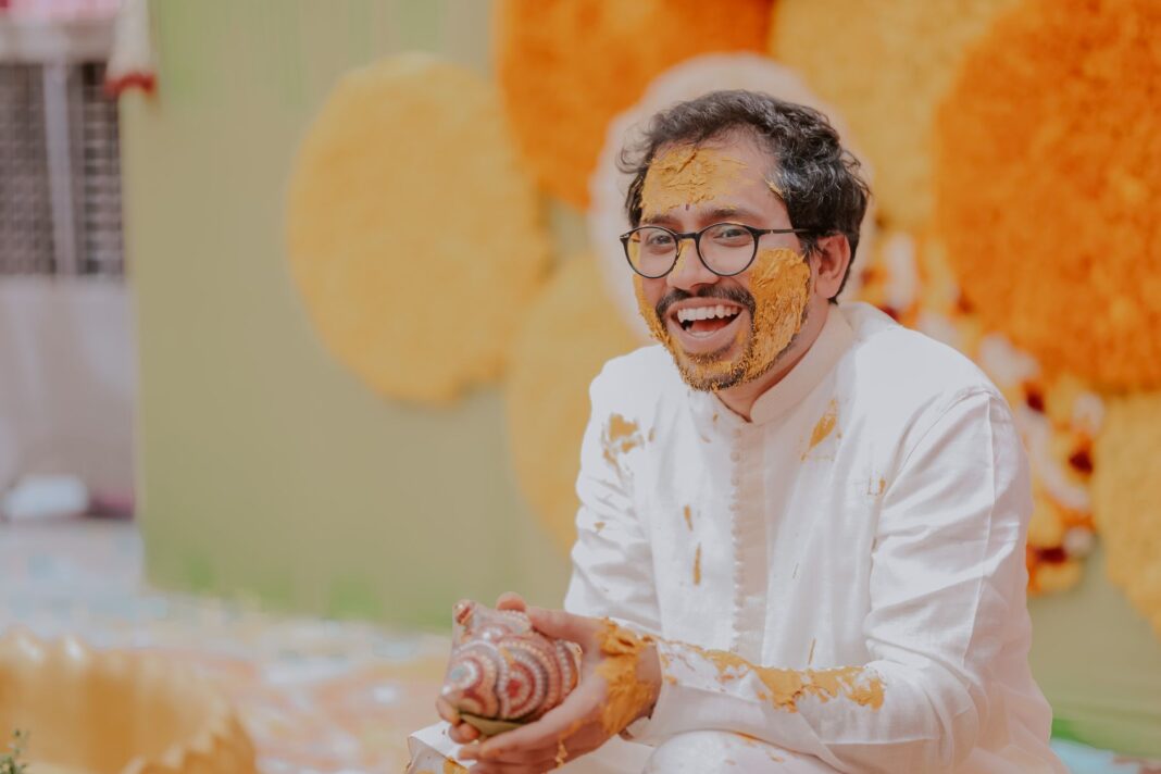 Roześmiany pan młody podczas ceremonii Haldi, pokryty kurkumą Roześmiany pan młody podczas ceremonii Haldi, pokryty kurkumą